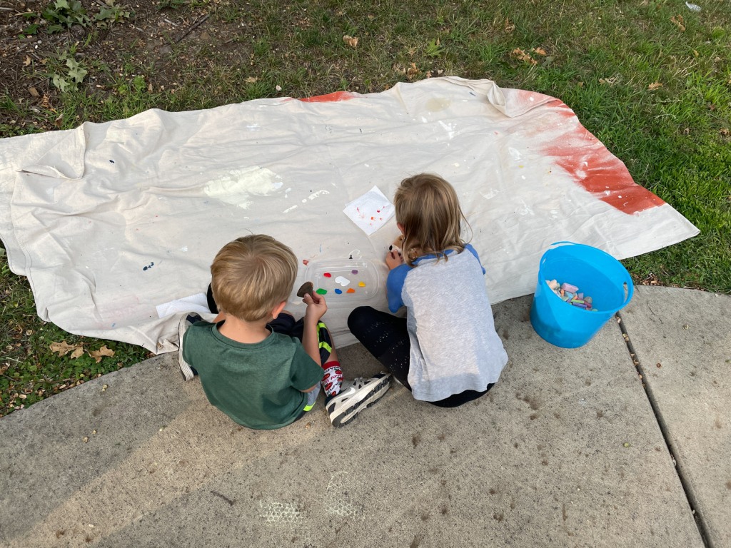 Two kids sitting on the ground and painting rocks.